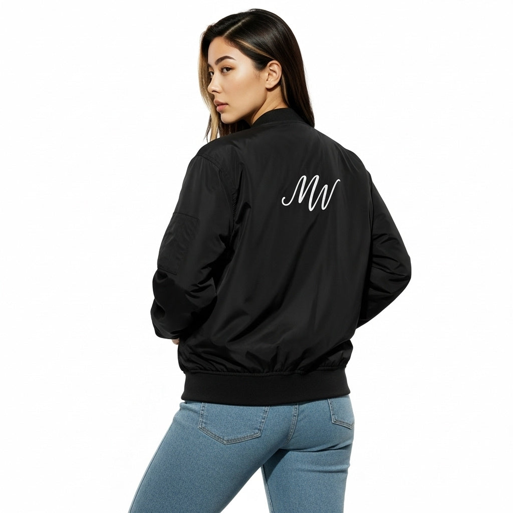 Person wearing a black bomber jacket with a logo on the back, standing against a white background